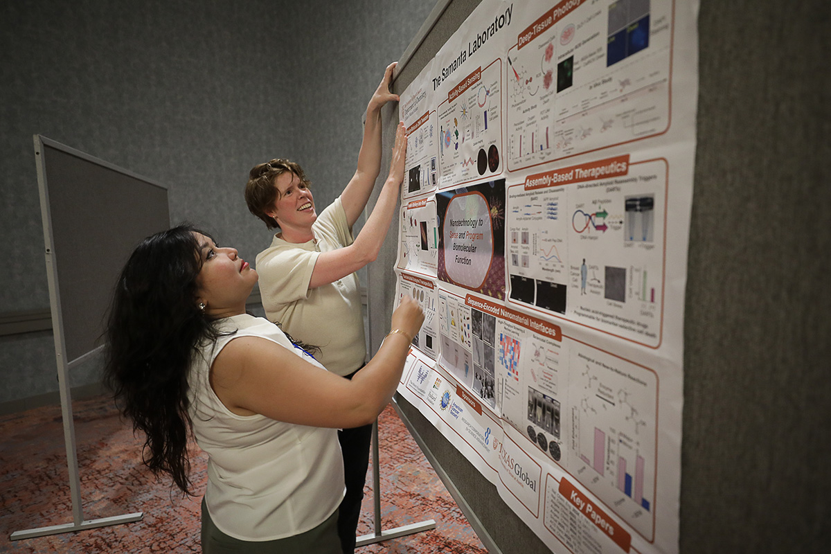two people hanging a large scientific poster on an easel at the 2026 Cottrell Scholars Conference